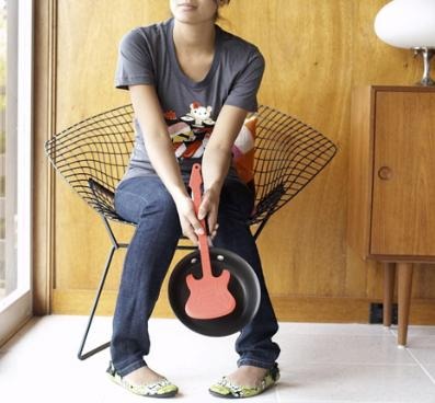 Girl holding a red flipper electric guitar spatula and a frying pan, pensively